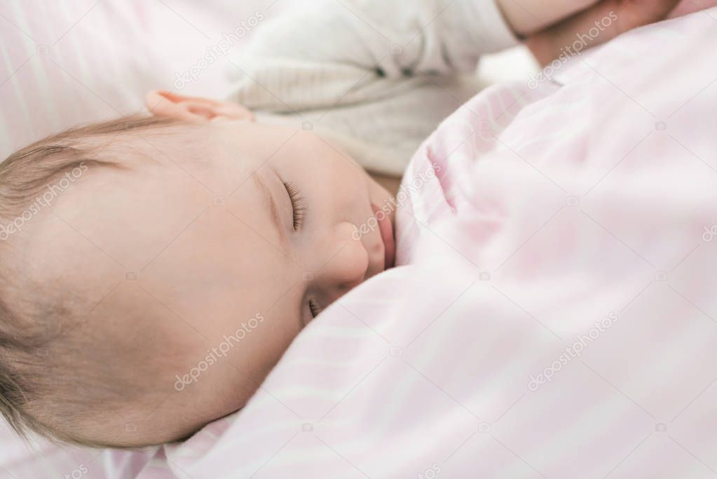 partial view of cute baby sleeping on mothers hands