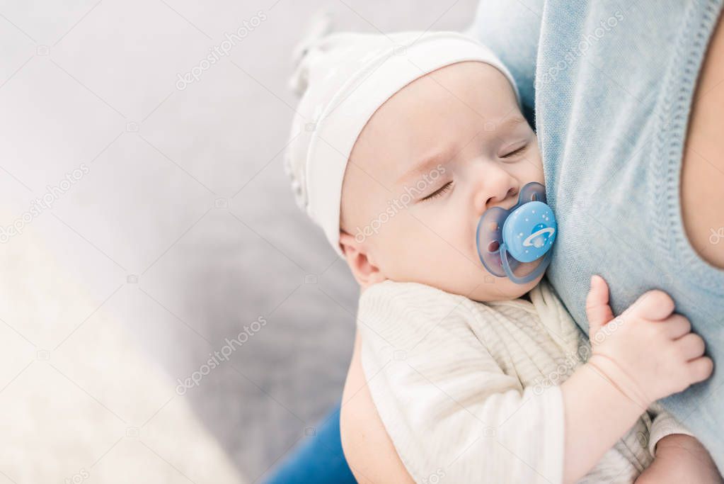 cropped shot of mother holding sleeping son with pacifier in hands