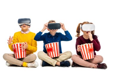 amazed kids with virtual reality headsets on heads holding striped carton buckets and eating popcorn isolated on white clipart