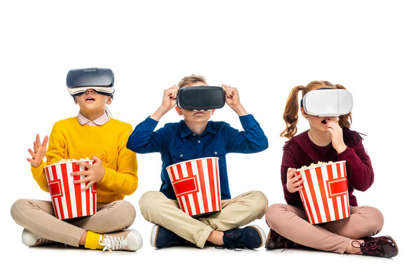 amazed kids with virtual reality headsets on heads holding striped carton buckets and eating popcorn isolated on white