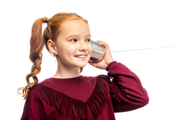 cute schoolgirl smiling and holding tin with rope near ear isolated on white