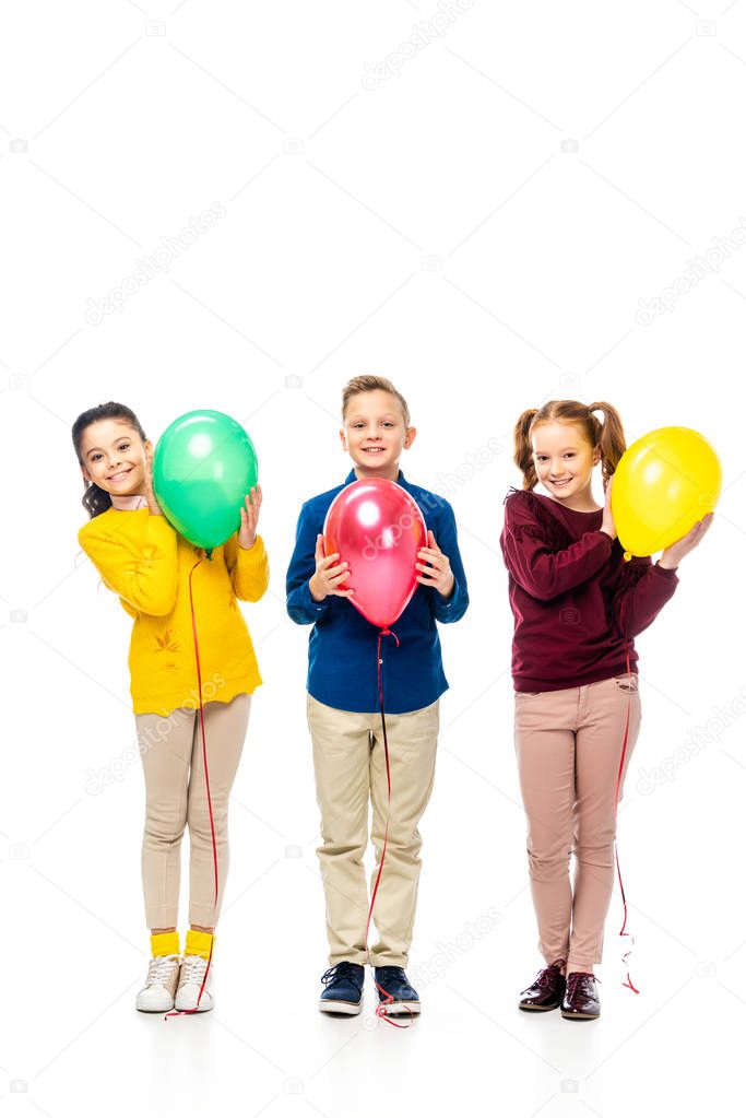 cute boy and schoolgirls smiling, holding multicolored balloons and looking at camera isolated on white