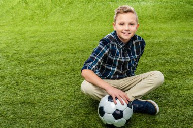 futbol topu yandan ile çimenlikte oturan ve kameraya bakarak çocuğun gülümseyen