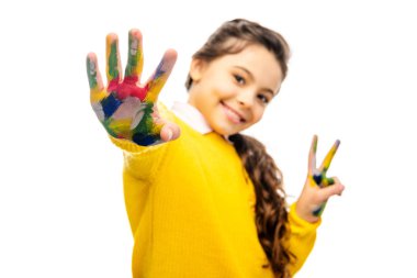 selective focus of smiling schoolgirl showing hand painted in colorful paints and looking at camera isolated on white clipart