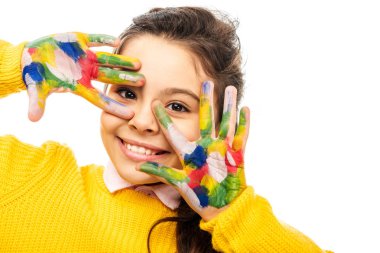 close up view of cute schoolgirl in yellow sweater smiling, looking at camera and showing hands painted in colorful paints isolated on white clipart