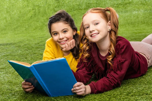 Colegialas Sonrientes Acostadas Césped Sosteniendo Libro Mirando Cámara —  Fotos de Stock