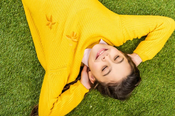 目を閉じての芝生で横になっている黄色いセーターのかわいい女子高生のトップ ビュー — ストック写真