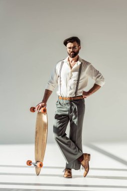 Longboard tutarak ve kameraya gri arka plan üzerinde seyir yakışıklı sakallı adam