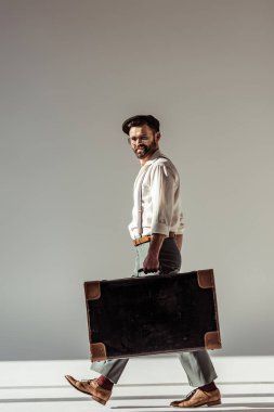 yakışıklı sakallı adam gözlük ve retro çanta ile yürüyüş ve gri arka plan üzerinde kameraya bakarak kap