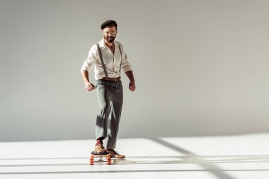 Longboard sürme ve kameraya gri arka plan üzerinde seyir yakışıklı sakallı adam