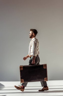 yakışıklı adam gözlük ve retro çanta ile gri arka plan üzerinde yürüme kap