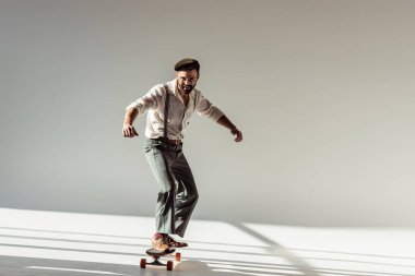 yakışıklı sakallı adam gözlük ve longboard sürme ve gri arka plan üzerinde kameraya bakarak kap