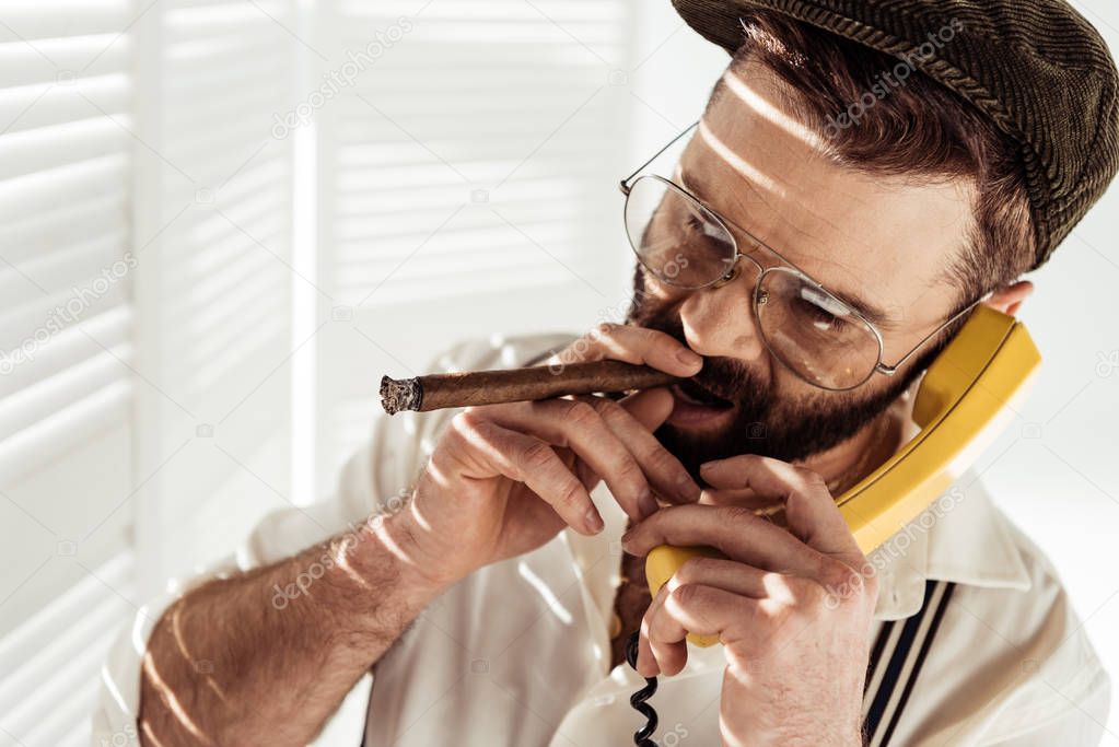 handsome bearded man in glasses talking on phone and smoking cigar 