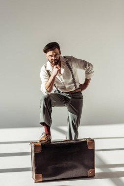 yakışıklı sakallı adamın yanına retro çanta ve kameraya gri arka plan üzerinde seyir