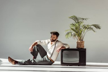 yakışıklı sakallı adam vintage yakın katta oturan şapkalı tv ile bitki pot ve kameraya arıyor