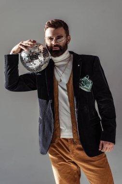 bearded man holding disco ball on shoulder and looking at camera isolated on grey clipart