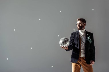 sakallı adam gri arka plan üzerinde mozaik disko topu elinde bakarak
