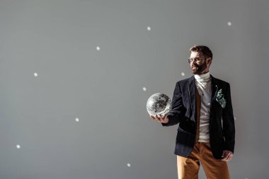 bearded man looking at mosaic disco ball in hand on grey background clipart