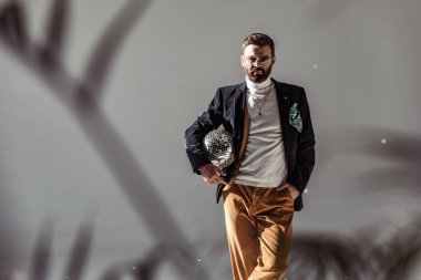 selective focus of bearded man holding mosaic disco ball and looking at camera on grey background clipart