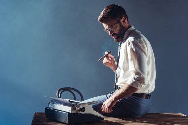 handsome man smoking and looking at typewriter clipart