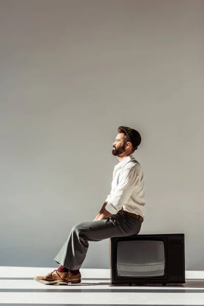 Вид Сбоку Красивого Бородатого Мужчины Сидящего Винтажном Телевизоре Сером Фоне — стоковое фото