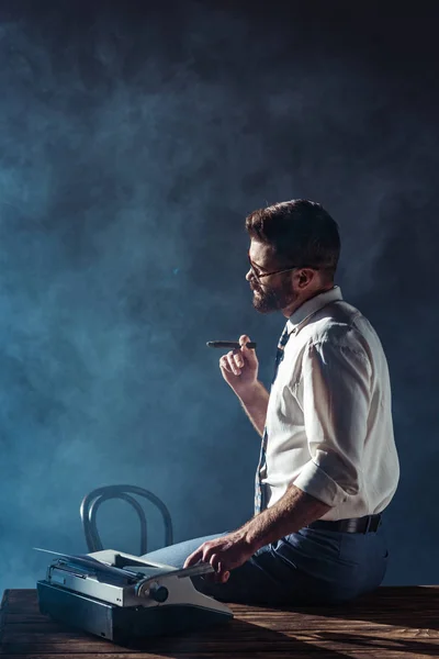 Schöner Mann Raucht Und Sitzt Auf Tisch Mit Schreibmaschine — Stockfoto