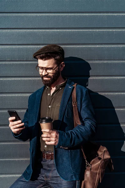 Homem Barbudo Bonito Óculos Tampa Segurando Copo Papel Usando Smartphone — Fotografia de Stock