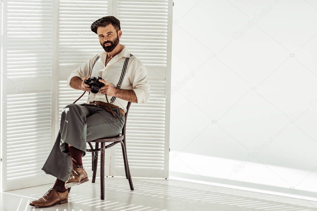 bearded stylish man sitting on chair with vintage film camera 