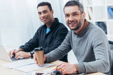 İşyerinde oturan ve kamera Office gülümseyen neşeli işadamları