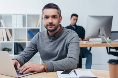 dizüstü bilgisayar kullanarak ve kamera Office bakarak yakışıklı işadamı