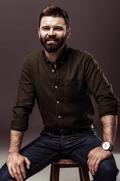 handsome smiling bearded man in brown shirt sitting on chair