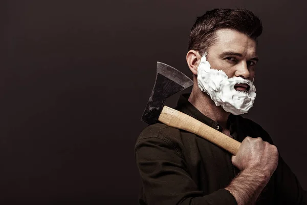 handsome bearded man in brown shirt holding axe and looking at camera isolated on brown