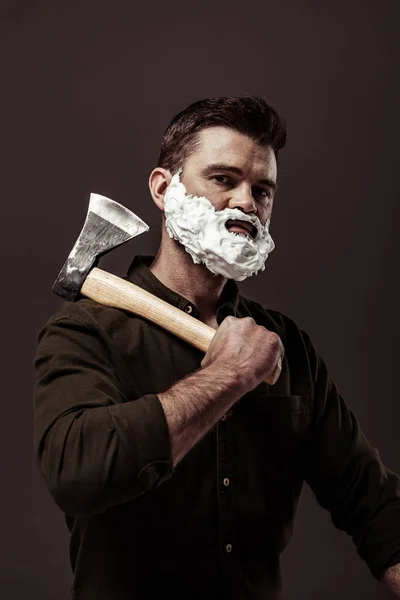 handsome bearded man in brown shirt holding ax while looking at camera isolated on brown