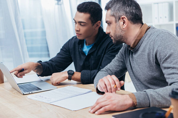 concentrated male coworkers using laptop and working together in office 