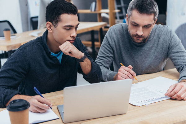 two focused business colleague taking notes and working with laptop in office