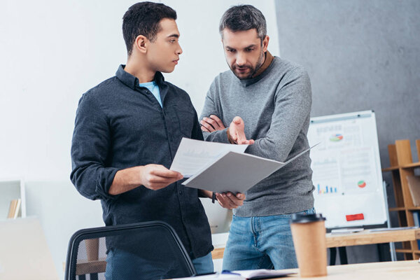 serious businessmen holding folder with papers and discussing project in office   