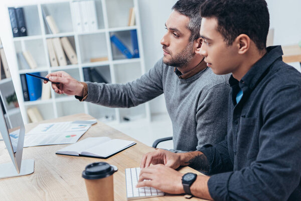 коллеги, печатающие на клавиатуре и указывающие на экран во время совместной работы с настольным компьютером
