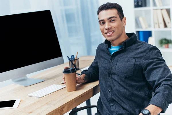 デスクトップ コンピューターを使用してカメラに笑顔コーヒーと青年実業家 — ストック写真