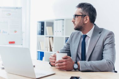 düşünceli işadamı kahve tutarak ve uzak işyerinde otururken seyir gözlük 