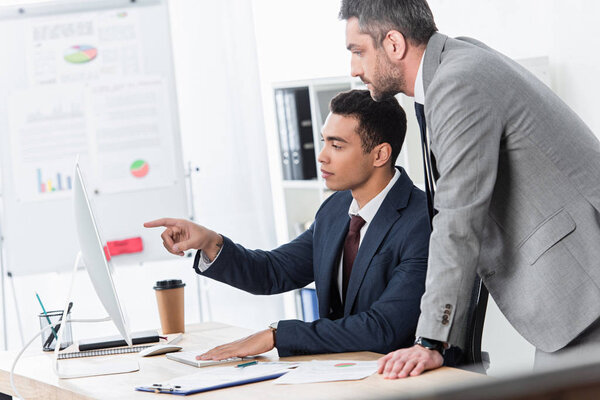 focused businessmen pointing with finger and looking at desktop computer in office