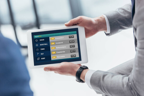 partial view of businessman holding digital tablet with sport bets app on screen