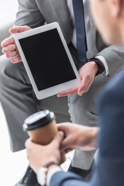 cropped shot of businessman showing digital tablet with blank screen to male colleague with coffee to go  