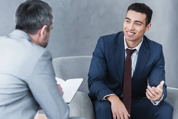 Jovem Empresário Sorrindo Conversando Olhando Para Colega Sentado Tomando Notas — Fotografia de Stock