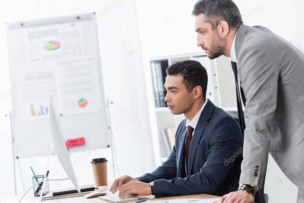 side view of serious businessmen working with desktop computer together in office