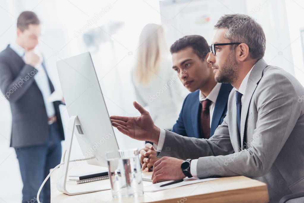 serious professional businessmen using desktop computer and discussing work in office