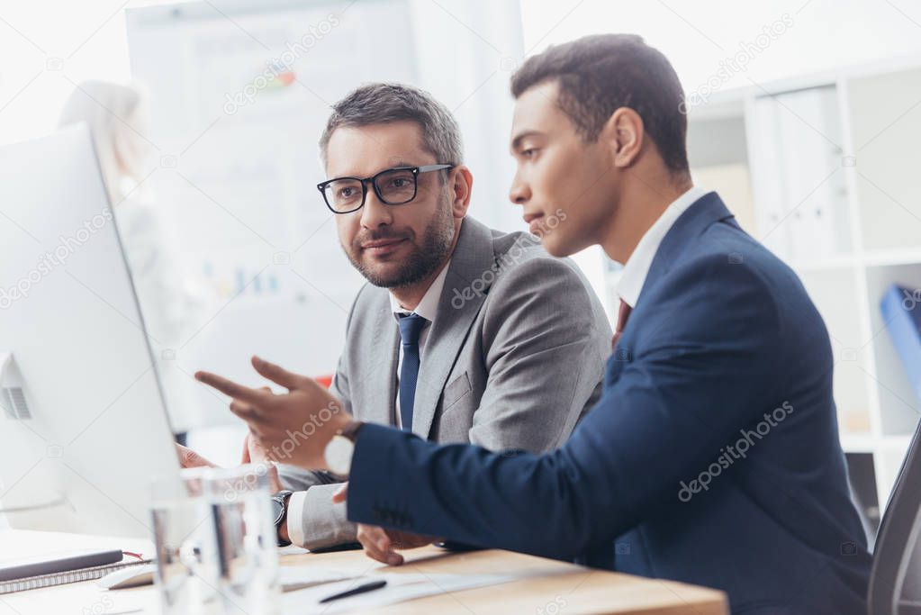 two professional businessmen discussing and using desktop computer in office 