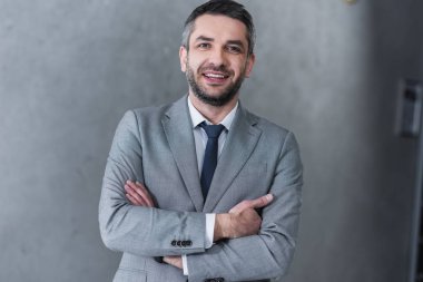 çapraz kolları ile ayakta ve kameraya gülümseyen emin yakışıklı işadamı