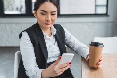 Git ve kullanma smartphone ofisindeki kahve tutan güzel genç iş kadını