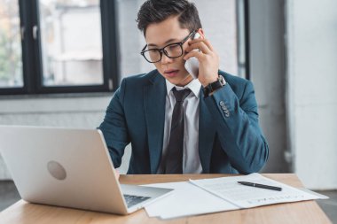 profesyonel genç Kazak işadamı smartphone ile konuşmak ve işyerinde dizüstü kullanarak gözlük
