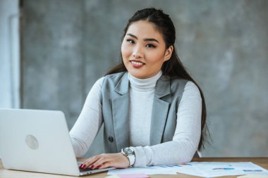 dizüstü bilgisayar kullanarak ve kamera Office gülümseyen güzel Asya iş kadını